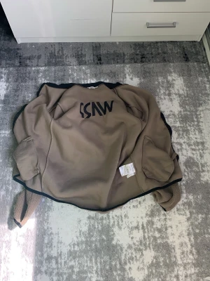 Brun fleecejacka från WARP - Mysig brun fleecejacka från WARP med svart kantband och stor logga på ryggen. Jackan har två fickor framtill och är tillverkad i mjukt teddyfleece-material som håller dig varm under kyliga dagar. Perfekt för lager-på-lager och enkel att matcha.