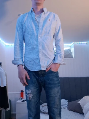 Blårandig skjorta från Ralph Lauren - Säljer en blårandig skjorta från Ralph Lauren i super slim fit. Skjortan har klassisk krage, knappar framtill och lång ärm. Tillverkad i bomull och har en liten broderad logga på bröstet.