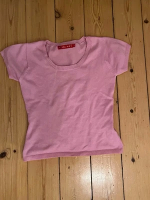 Ljusrosa topp från ICHI - Supersöt ljusrosa topp från ICHI med rundad halsringning och ribbade kanter. Kortärmad och i mjukt material som känns skönt mot huden. Perfekt att styla med jeans eller kjol för en fräsch look.