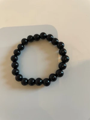 Svart pärlarmband med elastisk tråd - Snyggt armband med svarta, blanka pärlor trädda på elastisk tråd. Perfekt för dig som gillar enkel men stilren design. Passar till många olika looks och är lätt att ta på och av.