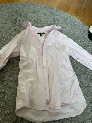 Ljusrosa skjorta från GANT - Säljer en klassisk ljusrosa skjorta från GANT i storlek 36. Skjortan har lång ärm, knappar framtill och en tidlös krage. Perfekt för en clean och stilren look. Tillverkad i mjuk bomull för skön känsla hela dagen. Den svarta fläcken på bild tre är maskara på spegeln🫣