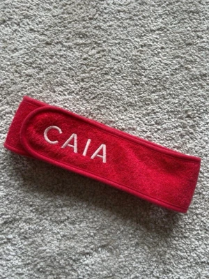Rött hårband från CAIA - Säljer ett rött hårband från CAIA med broderad vit logga.  Perfekt när du vill hålla håret borta vid sminkning eller hudvård.
