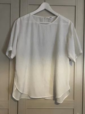 Vit blus med rund hals - Stilren vit blus med rund halsringning och korta ärmar. Blusen har en lös passform och lätt rundad nederkant som ger ett avslappnat intryck. Tillverkad i ett tunt, mjukt material som faller snyggt. Perfekt att matcha med jeans eller kjol.