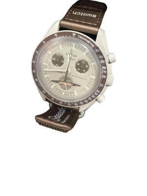 Omega x Swatch MoonSwatch brun - Säljer en Omega x Swatch MoonSwatch med brun textilrem och beige urtavla. Klockan har kronograf, tachymeter och flera subdials. Snygg kontrast mellan den ljusa boetten och den bruna ringen. Perfekt för dig som gillar ikoniska samarbeten.