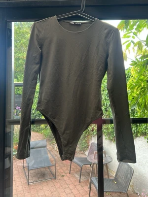 Grön långärmad body från Zara - Säljer en Grön  långärmad body från Zara med rund halsringning. Bodyn har en enkel och stilren design i mjukt stretchigt material som sitter snyggt på kroppen. Perfekt att matcha med jeans eller kjol för en clean look.