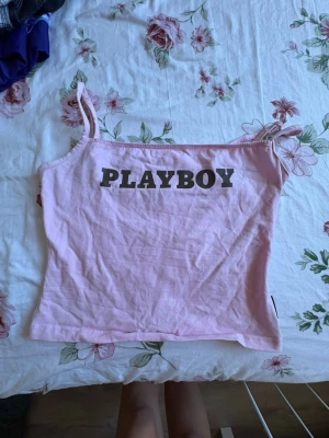 Rosa PLAYBOY linnetopp från Missguided - Säljer en ljusrosa linnetopp från Missguided med svart PLAYBOY-tryck framtill. Toppen har tunna axelband och är croppad i modellen. Perfekt för dig som vill ha en trendig och enkel topp till sommaren.