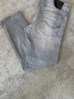 Ljusgrå raka jeans - Säljer ett par ljusgrå jeans med rak passform och klassisk femficksdesign. Jeansen har en diskret tvättad look och är tillverkade i ett mjukt denimtyg som känns bekvämt. Perfekta för dig som gillar en clean och enkel stil.