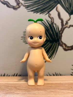 Sonny Angel Fruit Series figur - Söt samlarfigur från Sonny Angel Fruit Series. Dockan är beige med stora svarta ögon och har ett grönt blad på huvudet. Tillverkad i plast och kommer med originalförpackning. Perfekt för dig som gillar unika minifigurer och vill ha något gulligt till hyllan.