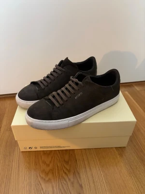 Axel Arigato Clean 90 Suede - Axel Arigato Clean 90 Suede – Dark Brown/White – strl 43  Axel Arigato Clean 90 i mörkbrun mocka med vit sula och guldfärgad logotyp.  Klassisk minimalistisk modell tillverkad i premium mocka. Skorna är använda och har normala bruksspår, framför allt på sulorna/sulkanterna. Mockan är fortfarande i fint begagnat skick. Se bilder för exakt skick.  Originalkartong medföljer.  Modell: Clean 90 Suede Sneaker Färg: Dark Brown/White Storlek: EU 43 Nypris: ca 2 600 kr Pris: 999 kr
