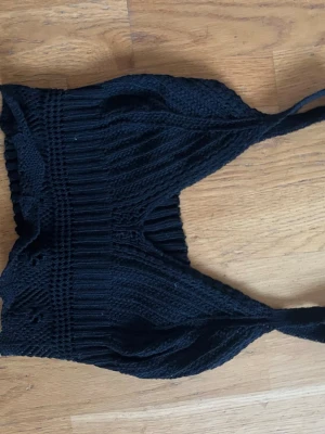Svart stickad croppad linnetopp - Köpt utomlands! Säljer en svart stickad linnetopp med ribbade detaljer och breda axelband. Toppen är croppad och har en snygg, figurnära passform som passar perfekt till höga jeans eller kjol. Perfekt för dig som gillar en enkel men trendig stil.