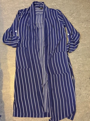Blåvit randig kappa Forever 21 - Lång, blå kappa från Forever 21 med vita vertikala ränder. Kappan har två stora fickor framtill och uppvikbara ärmar med knapp. Tunn och luftig, perfekt för lager på lager och en chill streetstyle-look.