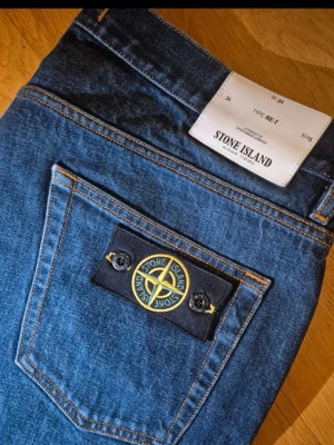 Blå jeans från Stone Island - Snygga blå jeans från Stone Island med klassisk femficksmodell och ikonisk patch på bakfickan. Jeansen har raka ben och är tillverkade i slitstark denim. Perfekta för dig som gillar streetwear och vill ha en clean look.Type RE-T