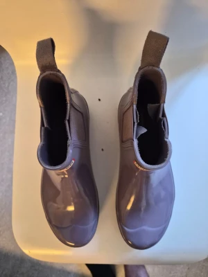 Lila Chelsea boots från Hunter - Snygga lila Chelsea boots från Hunter i glansigt gummimaterial. Klassisk siluett med elastiska paneler på sidorna och breda dragflikar bak. Perfekta för regniga dagar och ger en cool touch till din outfit.