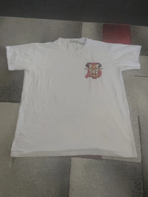 Vit t-shirt med broderad tjur - Vit t-shirt med korta ärmar och en broderad tjur i rött, svart och beige på bröstet. T-shirten har en klassisk passform och är gjord i mjuk bomull, perfekt för en avslappnad stil.