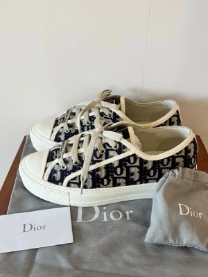 Dior Oblique låga sneakers - Säljer ett par Dior Oblique sneakers i tyg med klassiskt blått och vitt monogrammönster. Skorna har vita snören, gummisula och detaljer i vitt. Perfekta för dig som gillar exklusiv streetstyle och vill sticka ut med en ikonisk design.