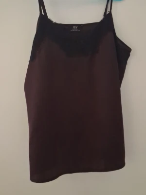 Mörk röd linnetopp med spets - Säljer en mörkbrun linnetopp från JDY med tunna axelband och spetsdetaljer vid urringningen. Toppen har en enkel och stilren design som passar perfekt till många olika outfits.