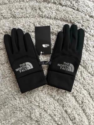 Svarta handskar från The North Face - Snygga svarta handskar från The North Face med logga på ovansidan. Handskarna har en stilren design och är perfekta för kyliga dagar. Tillverkade i ett mjukt och smidigt material som ger bra komfort och passform.
