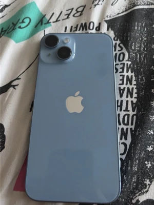 Blå Apple iPhone med dubbla kameror - iPhone 14 Snygg blå iPhone med stilren design och rundade hörn. Baksidan har två stora kameralinser och den klassiska Apple-loggan i mitten. Telefonen har en slät glasbaksida och metallram. Perfekt för dig som gillar modern teknik och vill ha en mobil som sticker ut. Jätte bra telefon utan några skador framsidan inga sprickor heller baksidan hel perfekt batterihälsan 76% och 128gb pris kan deskutieras 