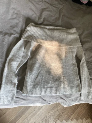 Beige off shoulder stickad tröja - Mysig beige stickad tröja med off shoulder-design och bred ribbad kant upptill. Tröjan har långa ärmar och ribbade muddar vid ärmslut och nederkant. Perfekt för dig som gillar en avslappnad men ändå trendig stil. Endast använd några gånger