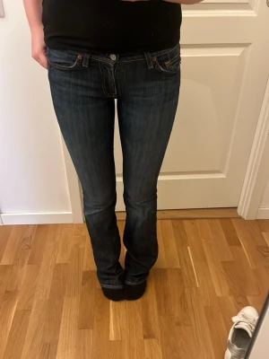 Mörkblå bootcut jeans från 7 all mankind - Säljer ett par mörkblå bootcut jeans med klassisk femficksmodell och orangea sömmar. Jeansen har låg midja och lätt utsvängda ben. Dessa är ifrån 7 all mankind som jag fick av min mamma. Säljs inte längre. Säljer då dessa är för långa för mig som äf 173cm. Pris går att diskutera 🤍