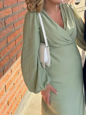 Ljusgrön långklänning med v-ringning - Snygg ljusgrön långklänning med v-ringad omlott överdel och långa puffärmar. Öppen rygg med knytning. Klänningen har en elegant och flowy passform, perfekt för dig som vill sticka ut med en stilren look. Materialet känns mjukt och följsamt mot kroppen. Nypris 999 kr 