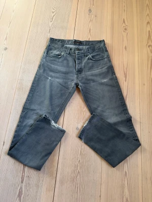 Grå jeans från Nudie Jeans Co - Säljer ett par grå jeans från Nudie Jeans Co med klassisk femficksmodell och raka ben. Jeansen har en snygg tvättad look och är tillverkade i denim. Perfekta för dig som gillar en avslappnad och stilren stil.