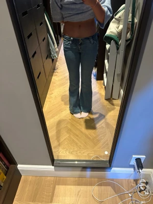 Blå bootcut jeans med låg midja - Säljer ett par blå bootcut jeans med låg midja och klassiska fem fickor. Jeansen har en snygg utsvängd passform och är tillverkade i denim med lätt stretch. Perfekta för dig som gillar retrovibbar och vill ha ett par jeans som sticker ut.