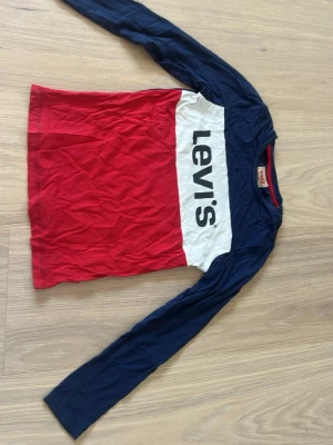 Levi's långärmad tröja i rött och blått - Snygg långärmad barntröja från Levi's med marinblå ärmar och överdel, röd nederdel och vit panel med stor logga framtill. 