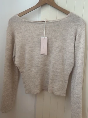 Beige stickad tröja med rund hals - En stilren beige stickad tröja med rund hals och långa ärmar. Tröjan har en mjuk och tunn stickning som passar perfekt till lager på lager. Enkel och tidlös design som är lätt att matcha med olika outfits.