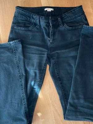 Svarta lågmidjade jeans med fickdetaljer - Säljer ett par svarta bootcut jeans med låg midja och snygga fickor bak med lock och knapp. Jeansen är i storlek 164🥰