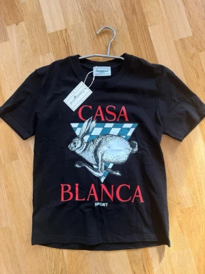 Svart t-shirt från Casablanca - Svart t-shirt från Casablanca med tryck av en hare och texten 'CASABLANCA SPORT' i rött framtill. T-shirten har rund hals och korta ärmar. Materialet är mjuk bomull och passformen är normal.