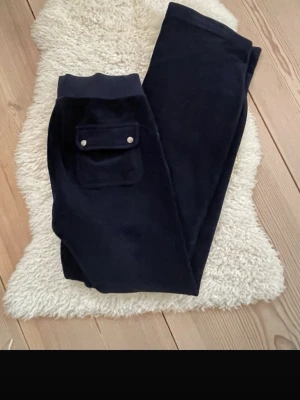 Mörkblå mjukisbyxor med fickor - Säljer ett par mörkblå mjukisbyxor i mjuk velour med raka ben och bred resår i midjan. Byxorna har stora fickor framtill, varav en med lock och tryckknappar. 