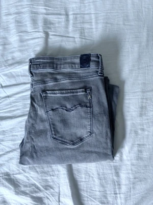 Grå jeans från Replay - Snygga grå jeans från Replay i klassisk femficksmodell. Jeansen har raka ben, diskreta slitningar och detaljerade sömmar på bakfickan. Tillverkade i mjukt denimtyg som ger en skön passform och stilren look.