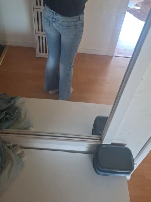 Ljusblå bootcut jeans med slitning - Säljer ett par ljusblå bootcut jeans med en liten slitning vid ena låret. Jeansen har klassiska fem fickor och är i ett mjukt denimtyg. Passar perfekt till dig som gillar en avslappnad men trendig look.