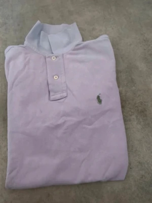 Ljuslila pikétröja med krage - Säljer en ljuslila pikétröja med klassisk krage och korta ärmar. Tröjan har knappar framtill och en liten broderad logga på bröstet. Tillverkad i mjuk bomull för en bekväm känsla. Den är i storlek S, men passar som M. 