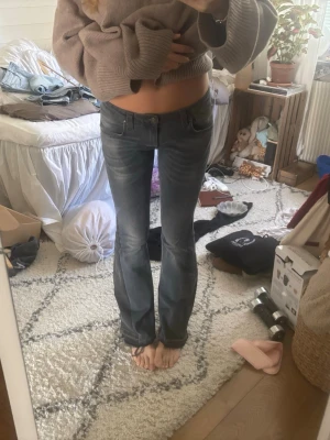 Mörkgrå bootcut jeans - Säljer ett par mörkgrå bootcut jeans med lätt slitningar och klassisk femficksmodell. Jeansen har låg midja och är tillverkade i ett stretchigt denimtyg som sitter snyggt på benen. Perfekta för en avslappnad och trendig look.
