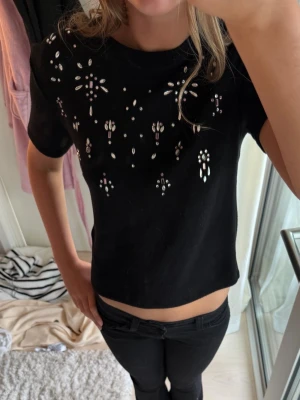 Svart t-shirt med paljettdetaljer - Snygg svart stickad t-shirt med paljettdetaljer/stenar på framsidan. Även lite kroppad.🩷