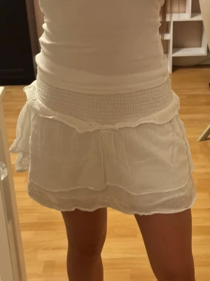 Vit volangkjol  - Vit kortkjol med volangdetaljer från Gina Tricot. Kjolen har ett luftigt och lätt tyg som passar perfekt till varma dagar. Den har flera lager och ger en flowy känsla.