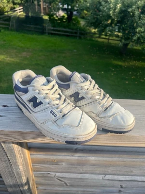 New Balance 550 - Säljer ett par klassiska New Balance 550 sneakers i vitt och marinblått. Skorna har retro basketstil med perforerade detaljer, tydlig logga på sidan och robust sula. Tillverkade i läder och textil med snörning framtill. Perfekta för dig som gillar streetwear. De är använda av en med smal fot. Kan behöva en noggrannare rengöring 🙈