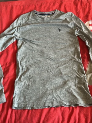 Grå långärmad tröja från Polo Ralph Lauren - Snygg grå långärmad tröja från Polo Ralph Lauren med klassisk broderad logga på bröstet. Tillverkad i mjukt och tunt material som passar perfekt till lager-på-lager. Enkel och stilren design som funkar till det mesta.