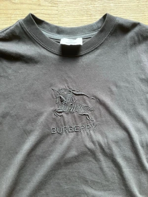 Svart Burberry t-shirt  - Snygg svart t-shirt från Burberry med broderad logga på bröstet. Klassisk rund hals och korta ärmar. Tillverkad i mjuk bomull för skön känsla. Perfekt för dig som gillar stilrena plagg med exklusiv touch. Väldigt skönt material och funkar i alla stilar. Köpt på farfetch för 3,2 för att de var rea. Kontakta för att diskutera pris. Använt typ tre ggr. Diskutera pris genom att skriva till mig. 