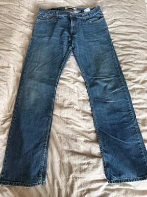 Blå raka jeans från Levi's - Klassiska blå jeans från Levi's med rak passform och fem fickor. Jeansen har en snygg tvättad look och är tillverkade i slitstark denim. Perfekta för en avslappnad stil och passar till det mesta i garderoben.