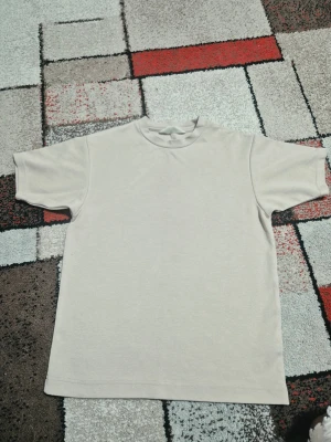 Två basic t-shirts i beige och ljusblå - Säljer två stilrena t-shirts i basic modell, en i beige och en i ljusblå. Båda har rund halsringning och korta ärmar. Perfekta att matcha med jeans eller shorts för en clean look. Materialet känns mjukt och skönt, troligtvis bomull.