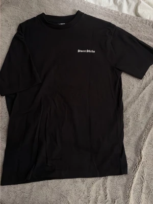 Svart Sweet SKTBS t-shirt med tryck på ryggen - Säljer en svart t-shirt från Sweet SKTBS med liten textlogga fram och stor palm- och textprint på ryggen. Större passform och rund hals. Perfekt för dig som gillar streetwear och grafiska tryck. Som nytt skick, endast använd fåtal gånger.