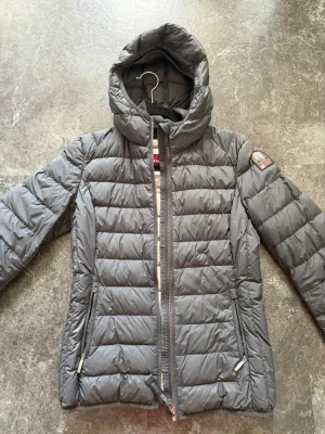 Svart parajumper jacka  - Snygg svart dunjacka med quiltad design och huva. Jackan har två dragkedjeförsedda fickor framtill och ett patch-märke på ena ärmen med texten 'PJS Anchorage'. Perfekt för kalla vinterdagar. Använd ett fåtalet gånger och är köpt för några år sedan därav finns inget kvitto längre. Det är barn storlek (Y-L) motsvarar ungefär en xs/s i vuxenstorlek