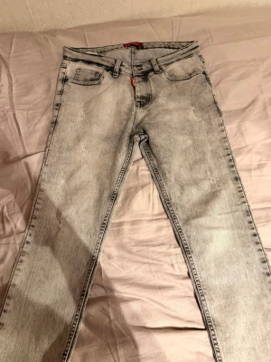 Ljusgrå tvättade raka jeans - Säljer ett par ljusgrå jeans med tvättad look och raka ben. Jeansen har klassisk femficksmodell, bälteshällor och knappgylf. Materialet är denim i bomull. Perfekta för dig som gillar en avslappnad och trendig stil.