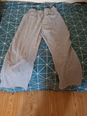 Gråa vida mjukisbyxor - Ett par gråa mjukisbyxor med bred passform och resår i midjan. Tillverkade i mjukt och bekvämt material, perfekta för chill dagar hemma eller när du vill ha det extra bekvämt. Klassisk enkel design utan synliga loggor eller detaljer.