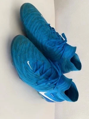 Blå Nike fotbollsskor med socka - Säljer ett par blå Nike fotbollsskor med högre strumpkrage för extra stöd runt ankeln. Skorna har en vit Nike-logga på sidan och mönstrad ovandel i syntetmaterial. Sulan är blå med greppvänliga dobbar, perfekt för spel på gräs.