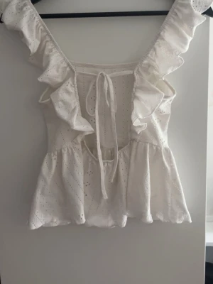 Vit blus med volang och knyt - Jätte snygg vit topp i bomull med detaljer och volang längs axelbanden. Toppen har en öppen rygg. Vet inte vart den är ifrån. Bra skick! Hyfsat tunn så bra till sommaren. Kom gärna med prisförslag!💗
