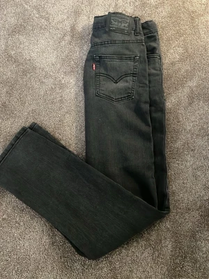 Svarta Levi's jeans slim taper fit. - Säljer ett par svarta jeans från Levi's med klassisk slim passform och fem fickor. Jeansen har en diskret tvättad look och Levi's ikoniska röda etikett på bakfickan. Perfekta till en grisch/ skön stil och tillverkade i mjukt denimtyg.